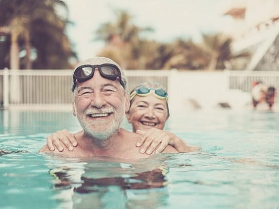 Ein altes Paar steht im Pool und lacht in die Kamera
