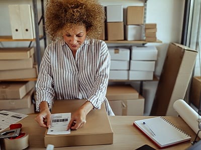 A woman in a striped gray shirt puts a shipping patch on a parcel