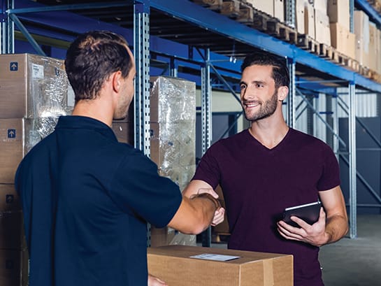 Zwei Männer stehen im Paketlager und geben sich die Hand.