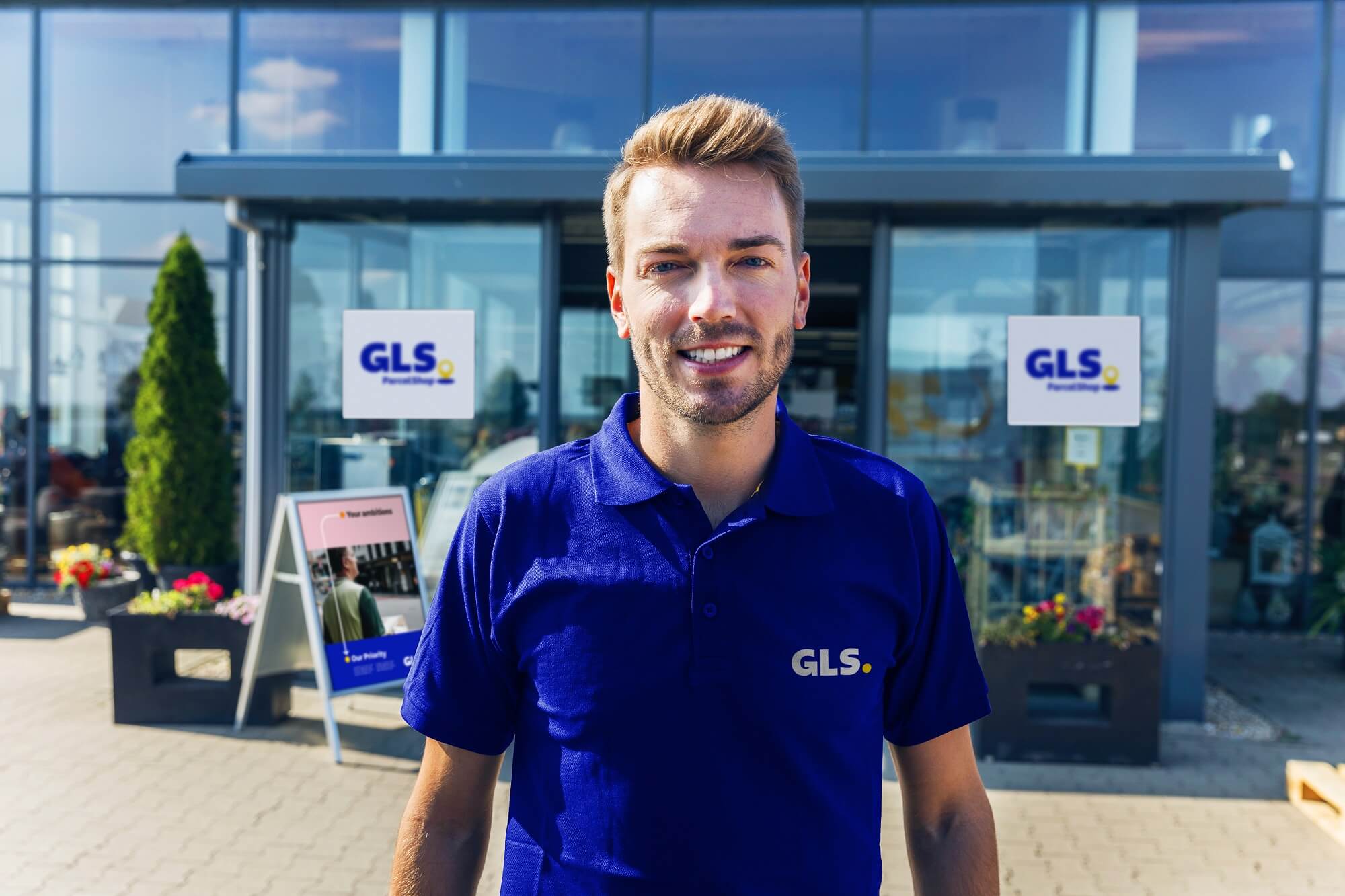 A GLS employee stands in front of a garden center that acts as a GLS parcel shop 