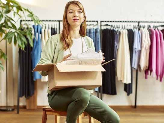 Eine Frau in einer Modeboutique packt einen weißen Sneaker in ein Paket zur Auslieferung ein