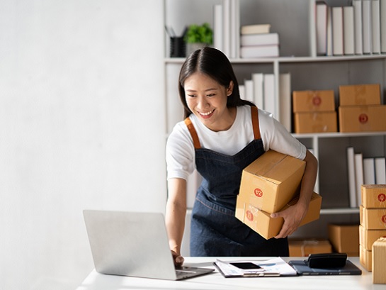 A woman in a fashion boutique wraps a white sneaker in a package for delivery