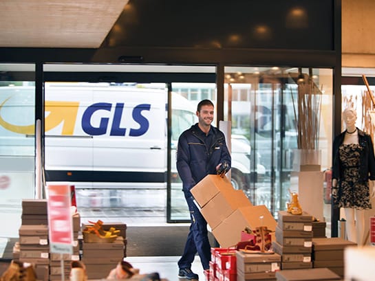 Ein GLS-Mitarbeiter liefert mit einem Transportwagen mehrere große Pakete an einen Fahsion Store