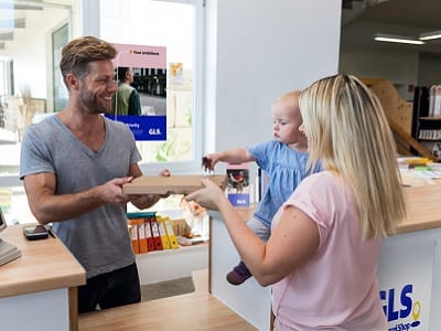 Frau mit Kind auf dem Arm holt Ihr Paket in einem GLS PaketShop ab