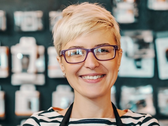Kurzhaarige blonde Frau steht in ihrem eigenen Laden an der Theke und lächelt freundlich