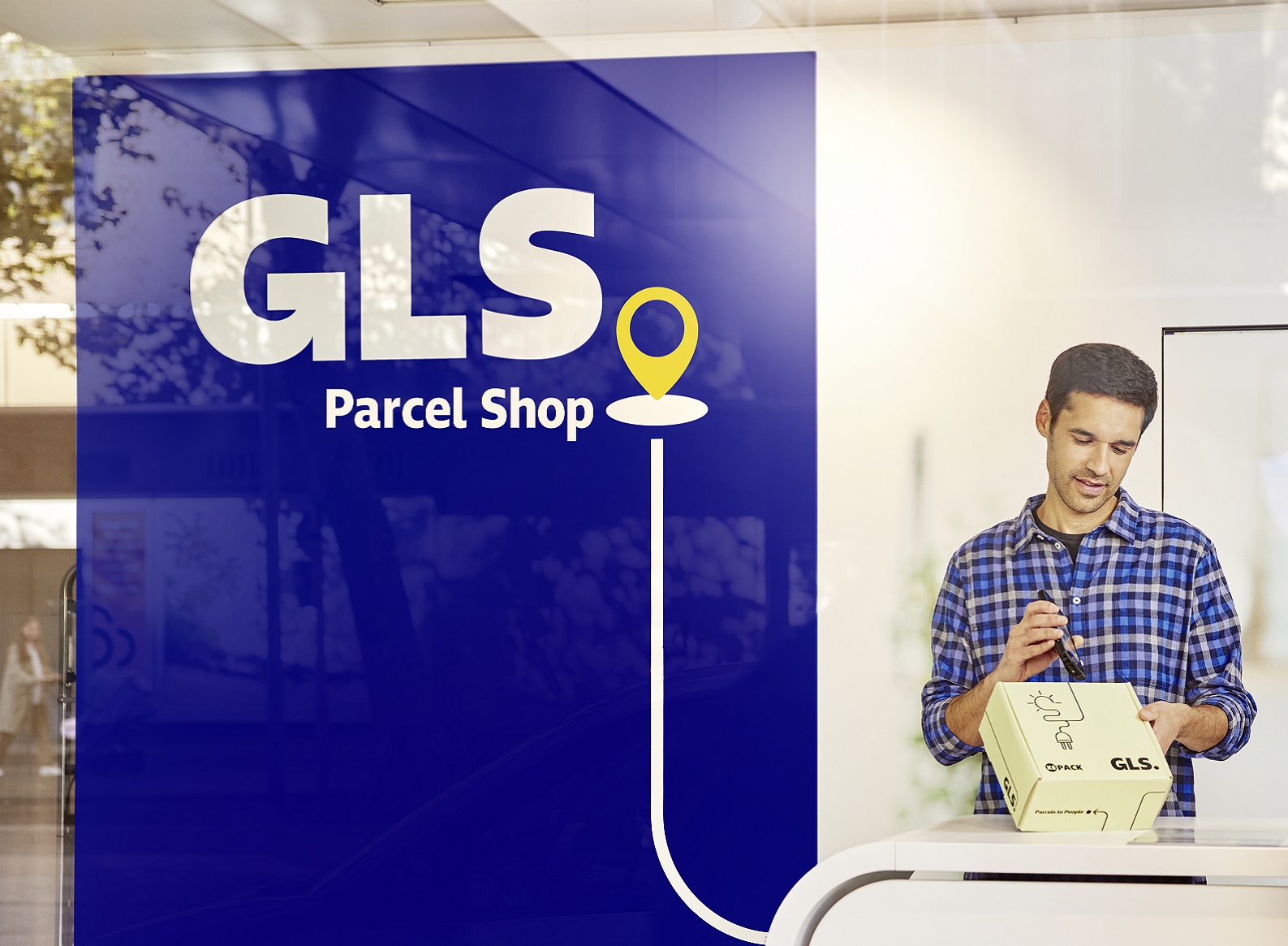 A man comes out of a GLS parcel shop carrying a package under his arm