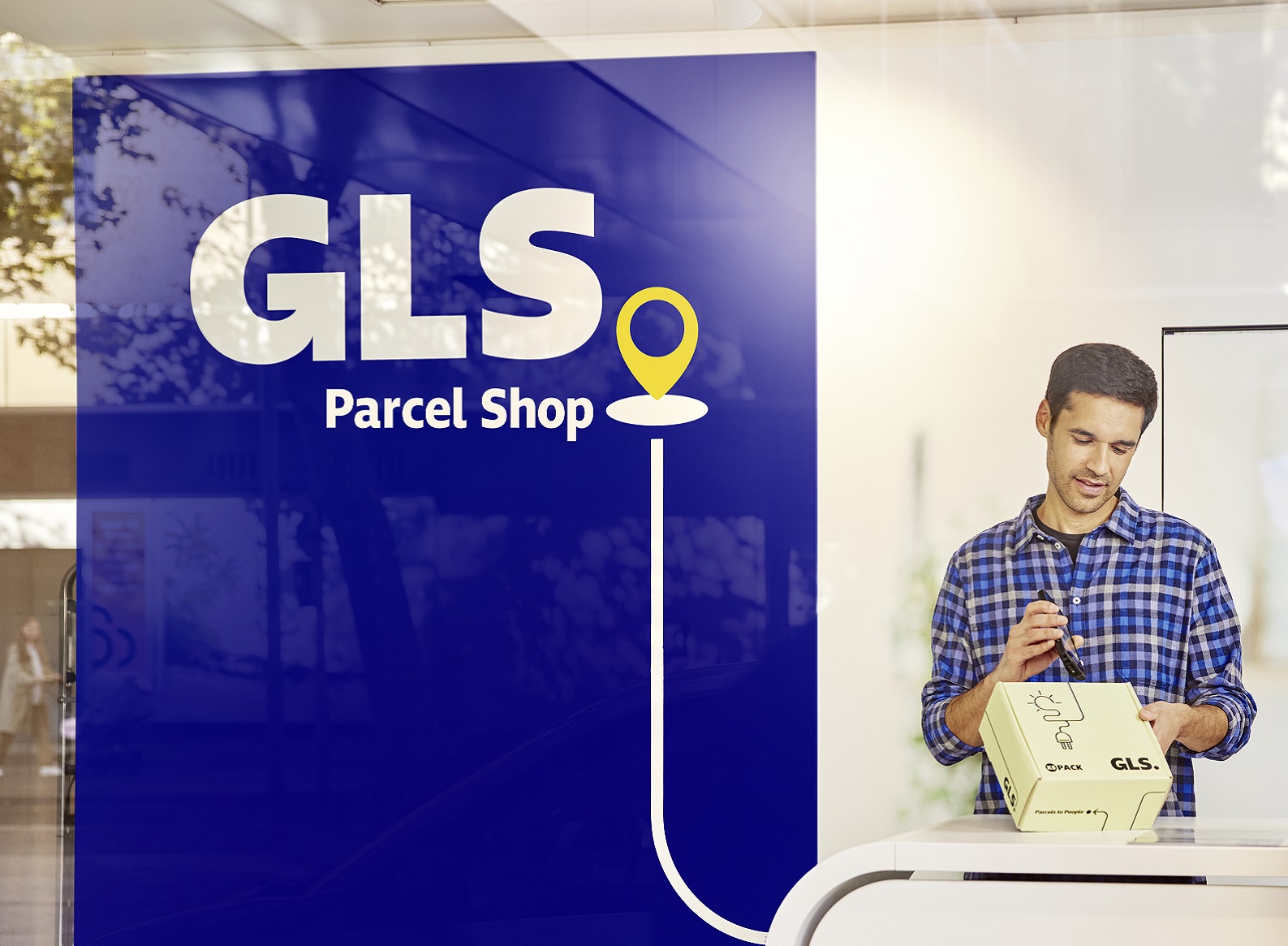 Ein GLS PaketShop-Betreiber steht in seinem Shop am Tresen und versendet ein Päckchen