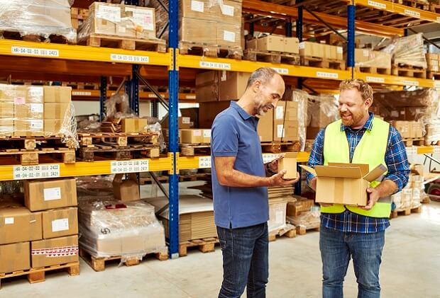 Two men stand in a parcel warehouse and exchange information about parcels of different sizes