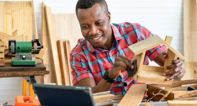 Ein Mann hat mit verschiedenen Teilen ein Haus aus Holz gebaut und zeigt stolz sein fertiges Endproduk