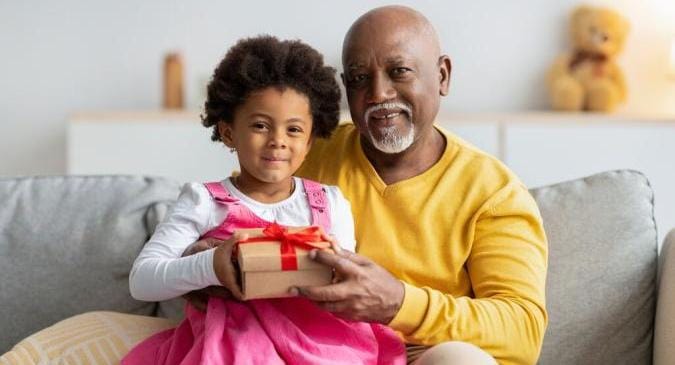 Ein Opa und seine Nichte sitzen auf dem Sofa und halten ein Geschenk