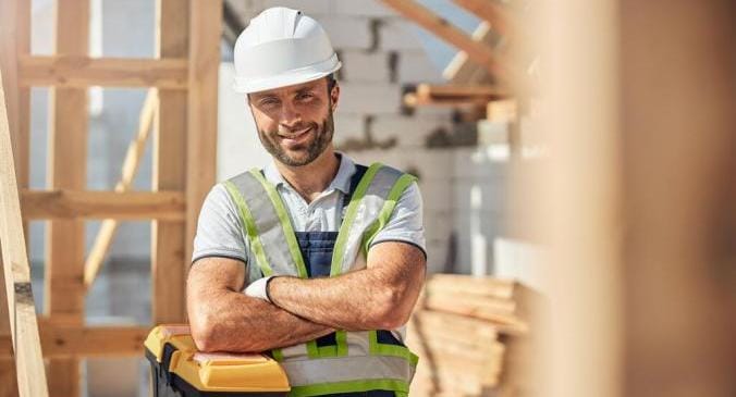 Ein Baumeister steht stolz vor seinen ganzen Rohstoffen aus Holz