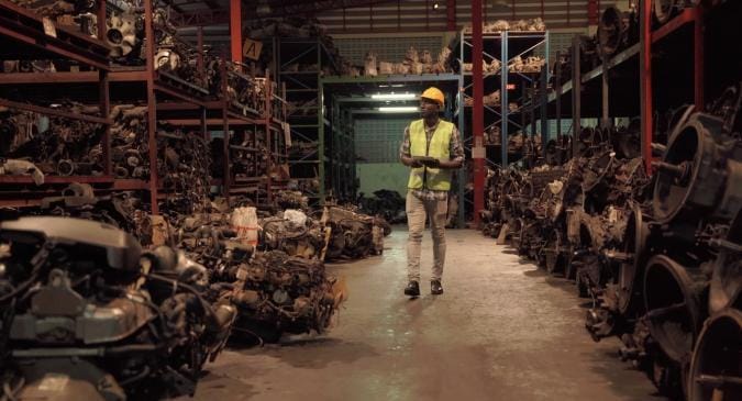 A man is standing in a large warehouse with many engines and gearboxes around him.
