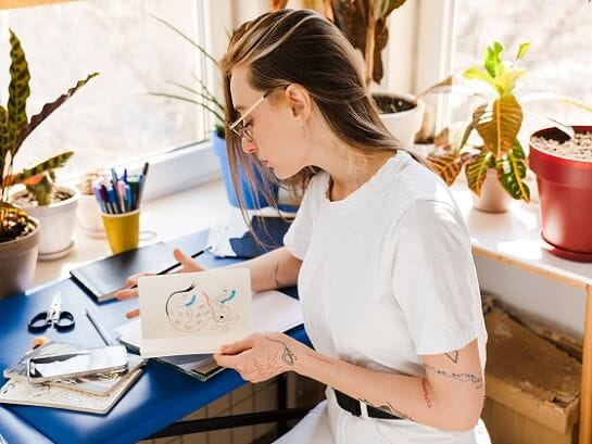 A woman with a tattooed arm holds a self-made card in her hand, which she wants to send with GLS