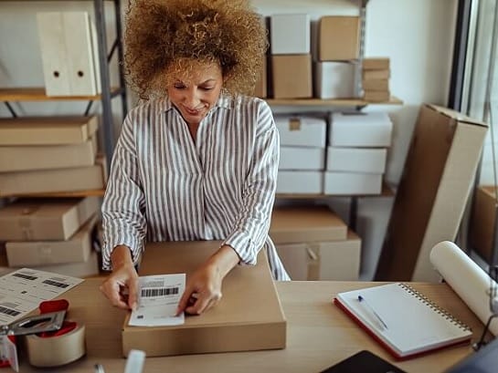 Frau verpackt Paket und klebt Paketlabel