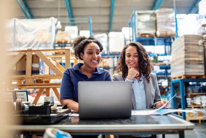 In the warehouse, two women work together at the PC to go through the professional shipping solution for frequent shippers, in the ShipIT shipping system