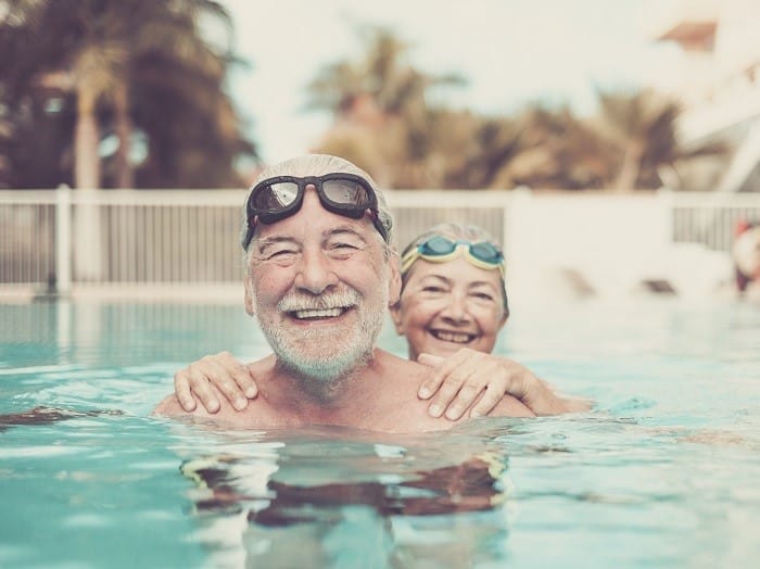 Old couple standing in the pool laughing at the camera