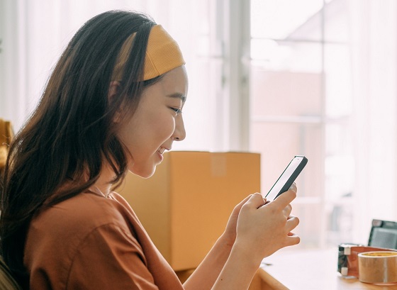 A young woman with dark long hair sits on the windowsill and surfs with her tablet on the GLS package page